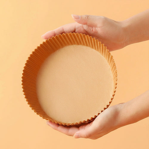 Hand holding a round air fryer paper tray against an orange background.